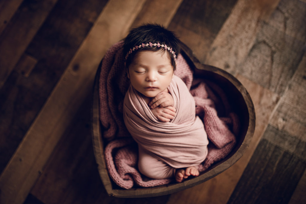 Photo of a newborn baby wrapped in pink in a heart shaped bowl.