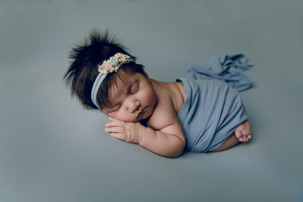 Photo of a baby girl curled up for a newborn shoot on blue background