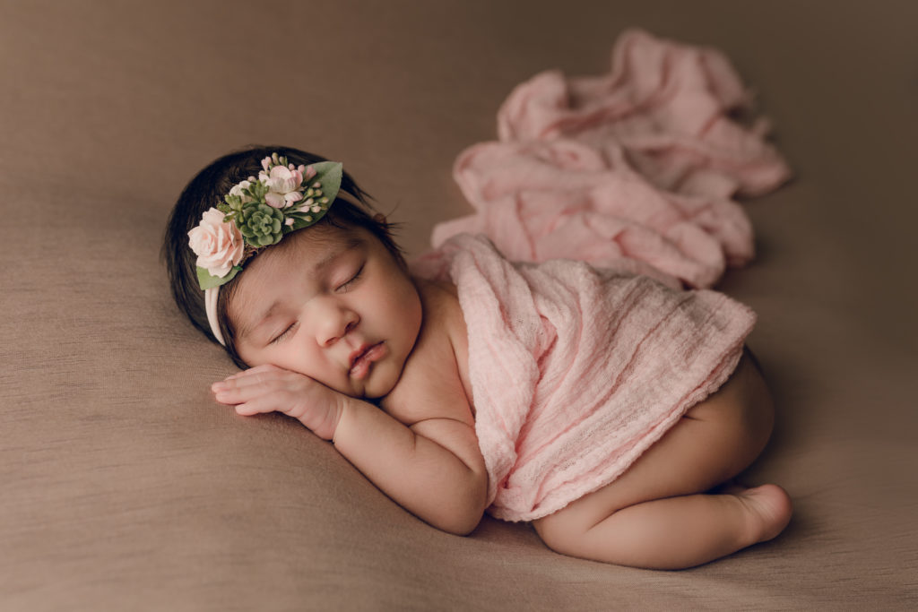 Newborn baby girl posed during a newborn photography session with pink and brown blankets