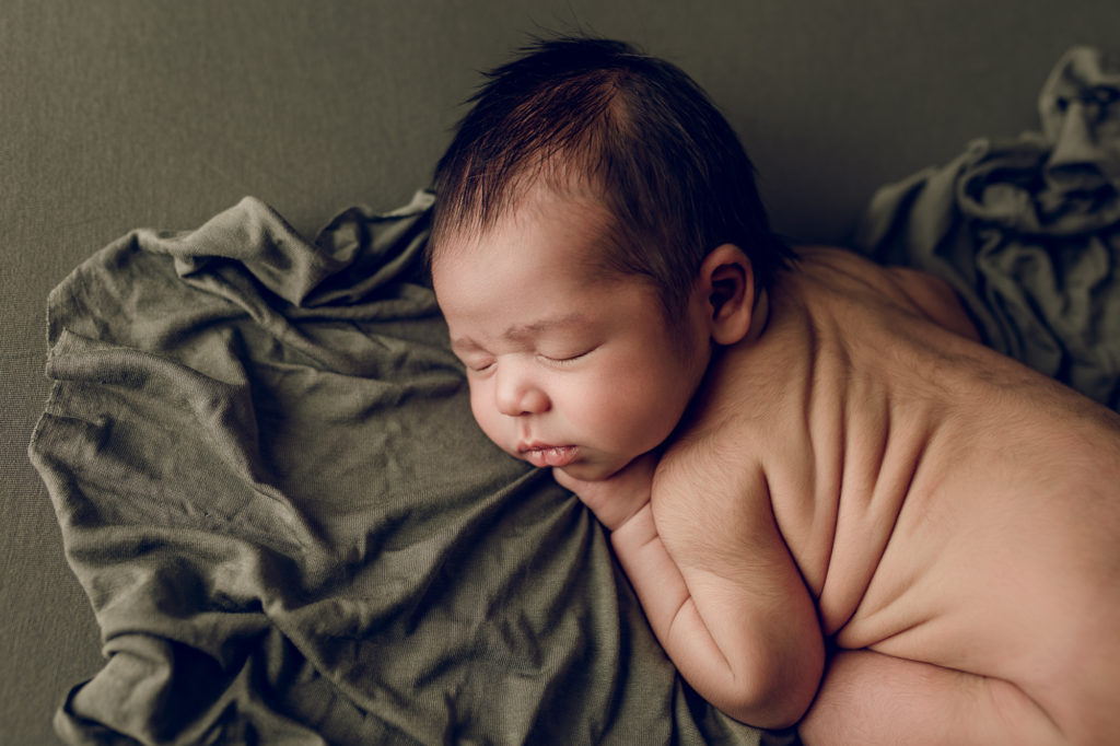 Newborn baby unwrapped posed for photography session, on green blanket