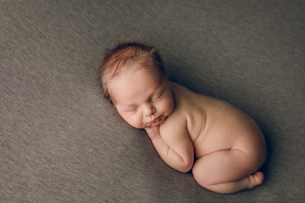 Newborn baby in a cute pose on a gray backdrop during a newborn photography session