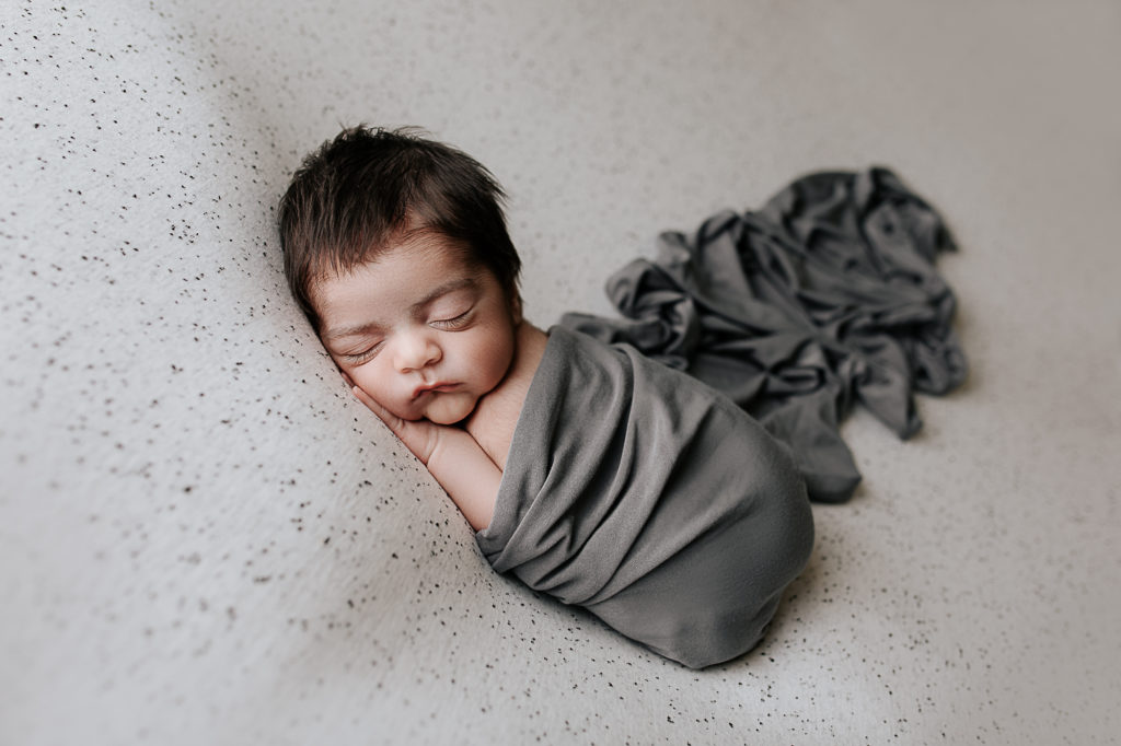 baby posed during a newborn photography session with a gray wrap 