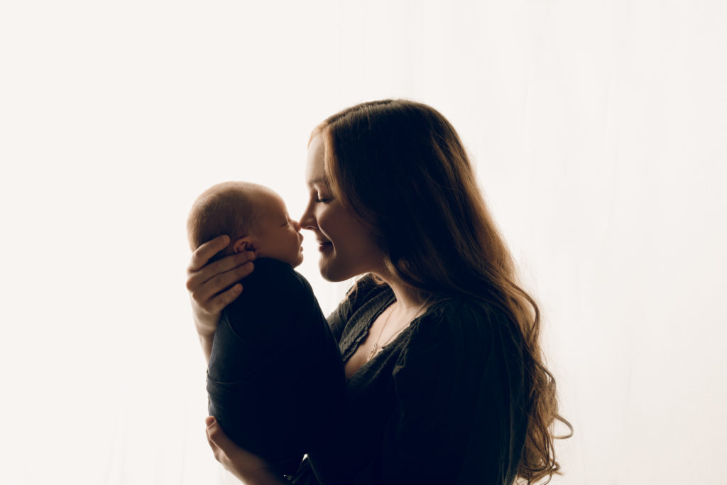 Mom and newborn baby in front of a window during a newborn photography session