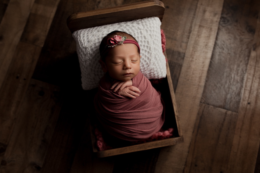Newborn baby girl in pink in a bed during a newborn photography session