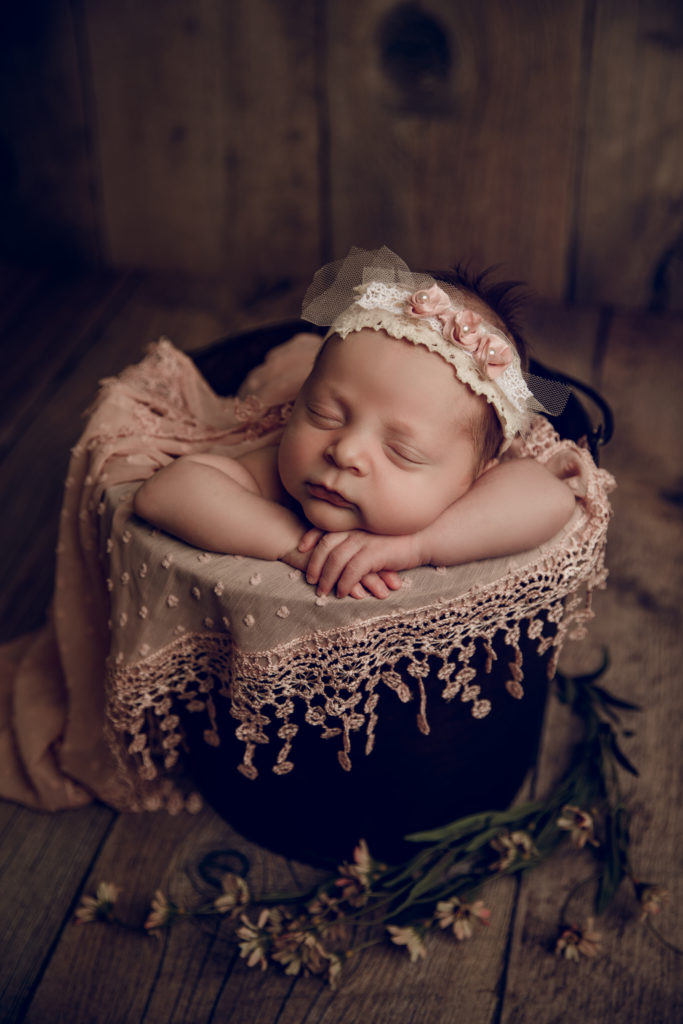 Newborn baby girl in pink in a bucket during a newborn photography session