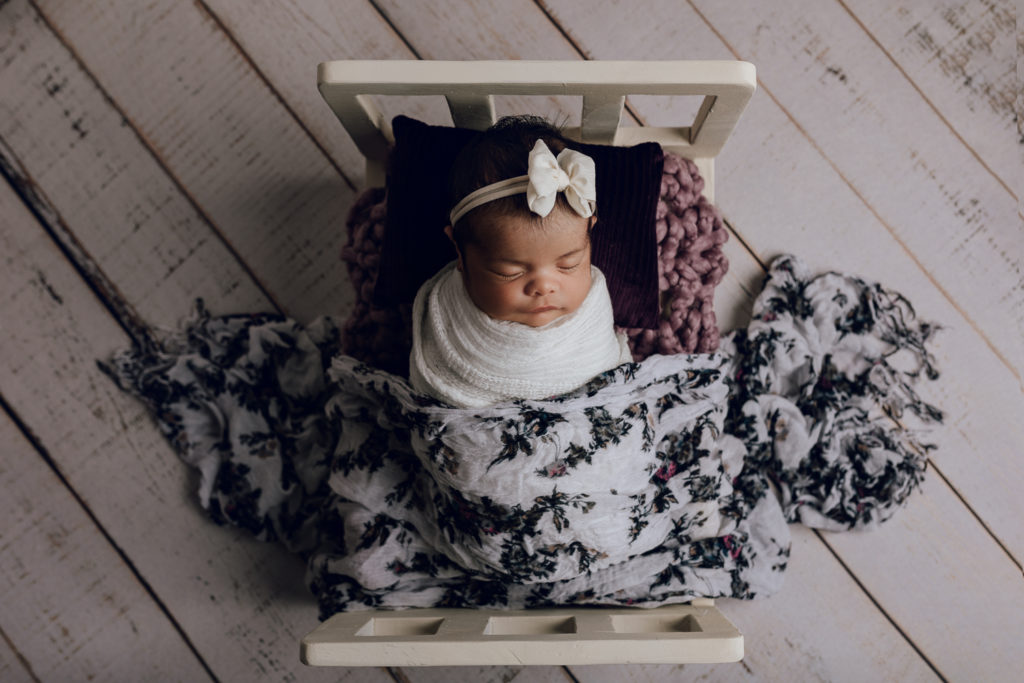 Baby girl in a tiny baby bed during a newborn photography session
