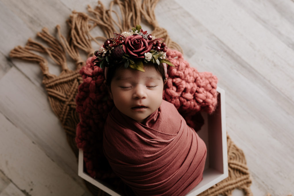 Newborn baby girl in pink in a octogon box during a newborn photography session