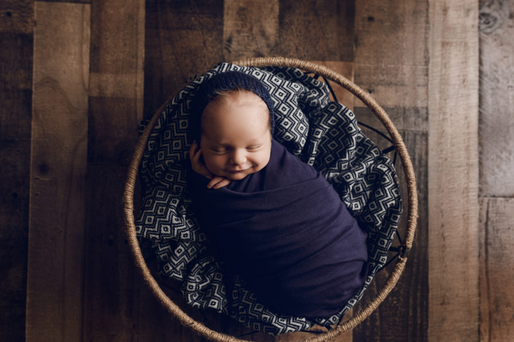 Newborn baby boy in blue in a round basket during a newborn photography session