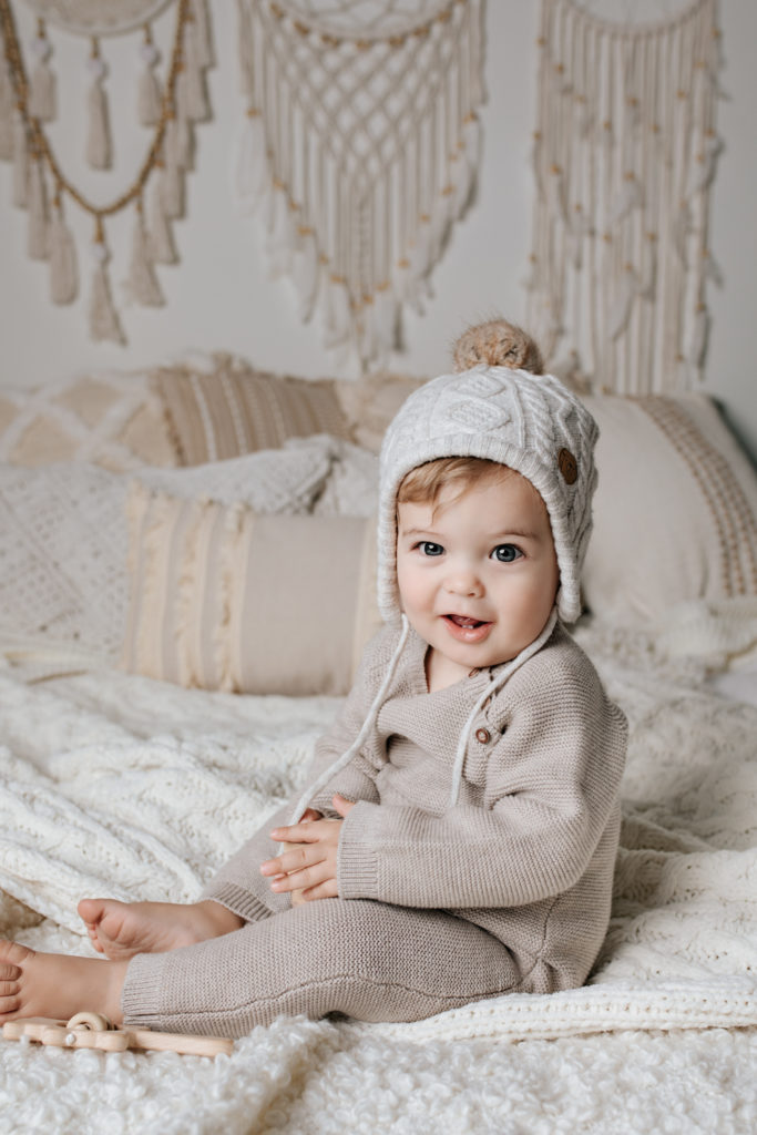 Baby boy wearing cream and sitting in a white bed during his cake smash portrait session.
