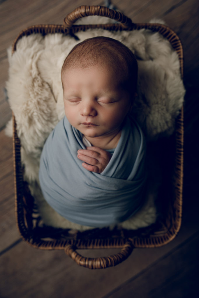 Newborn baby boy in blue in a basket during a newborn photography session
