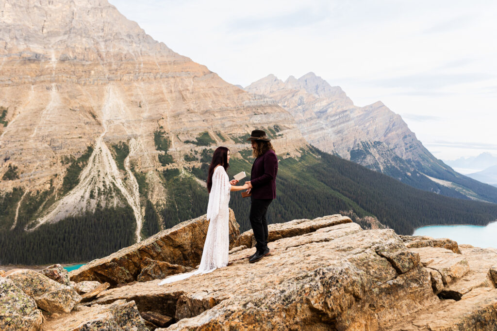 Couple is exchanging vows with a picturesque view of a blue lake below. They chose to elope in Banff National park.