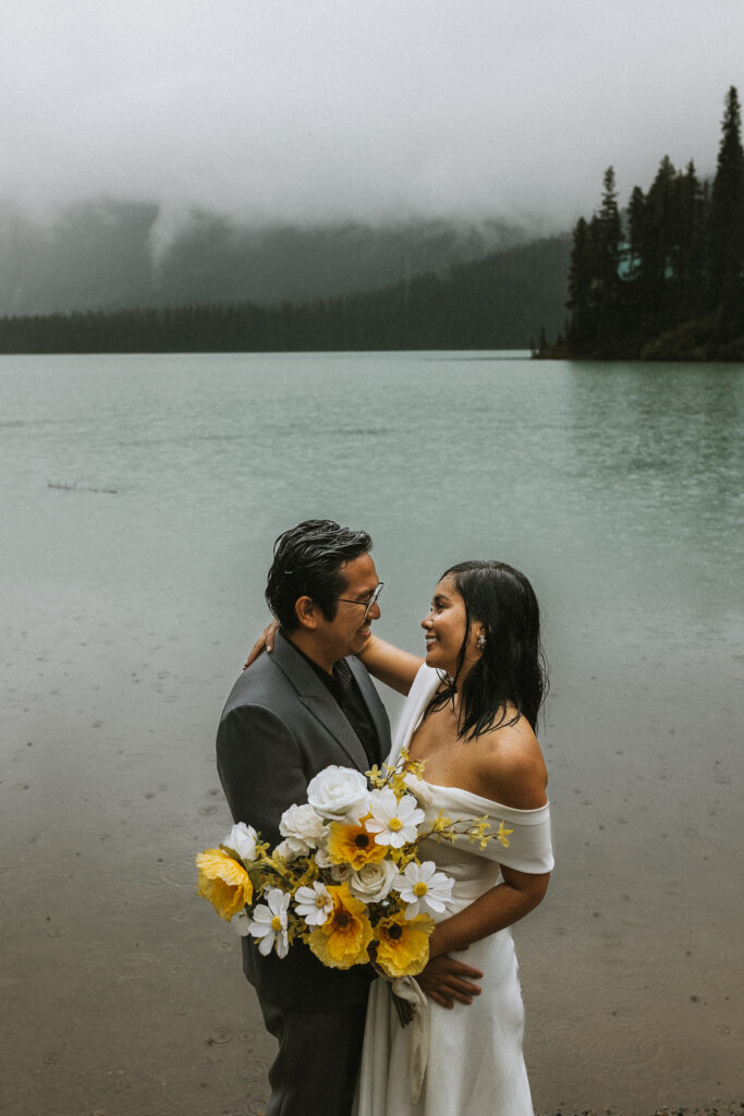 Bride and groom exchange vows on the lakes edge in Banff Canada. They just eloped and are enjoying the rain.