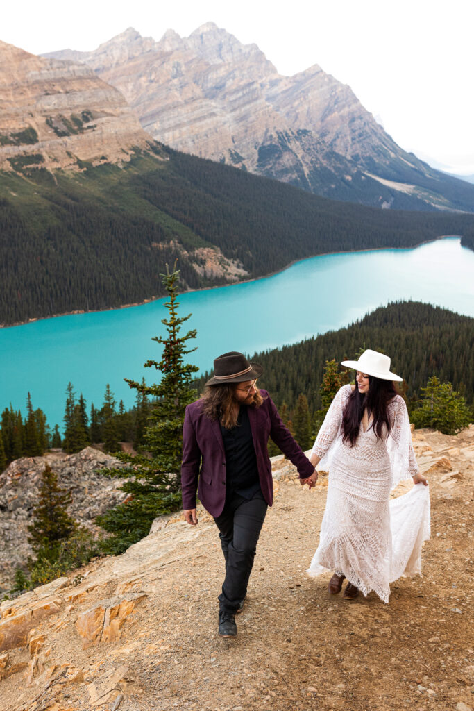 This couple is going on a short hike. They are at the top of a mountain that overlooks an amazing blue lake.